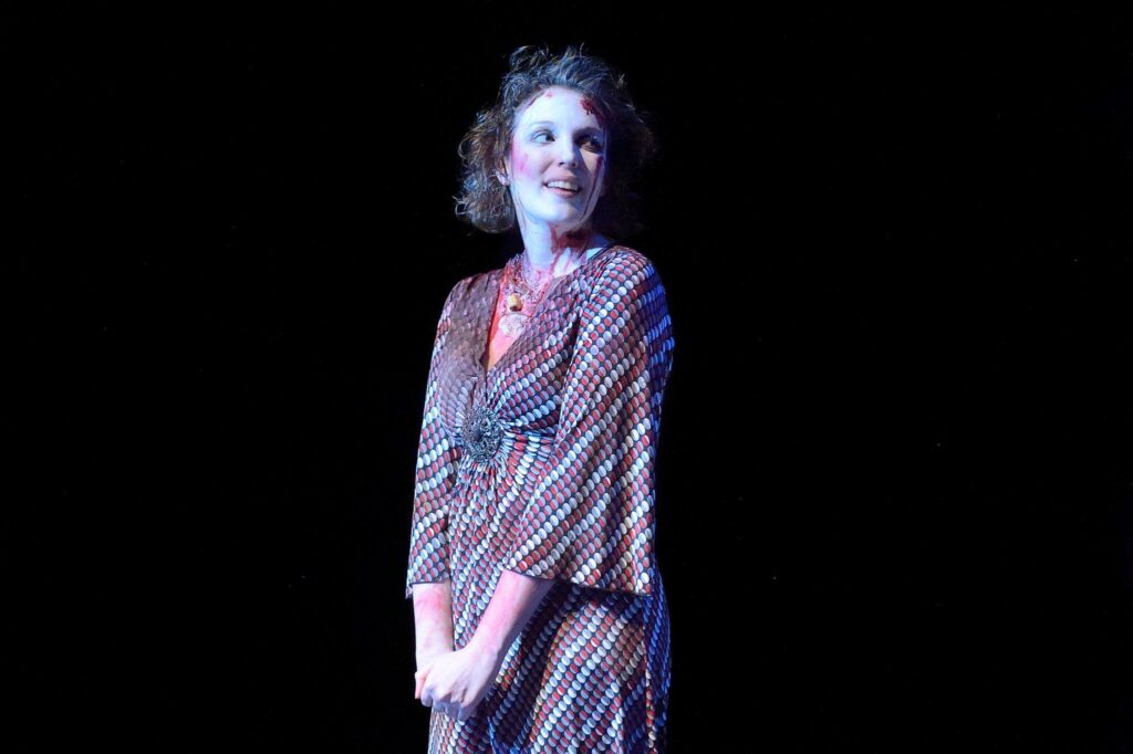 Woman in a dress and zombie make-up looking off-camera.