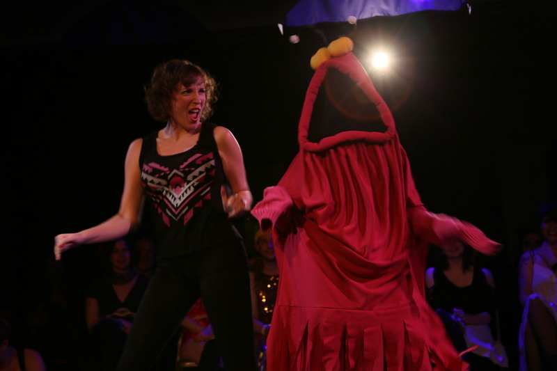 Two performers dancing on stage. Performer on the right is wearing a Yip Yip Martian costume.