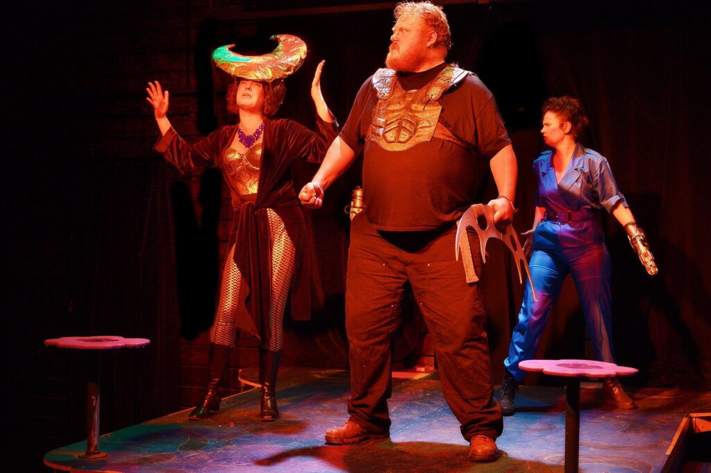 3 actors on stage in futuristic costumes.