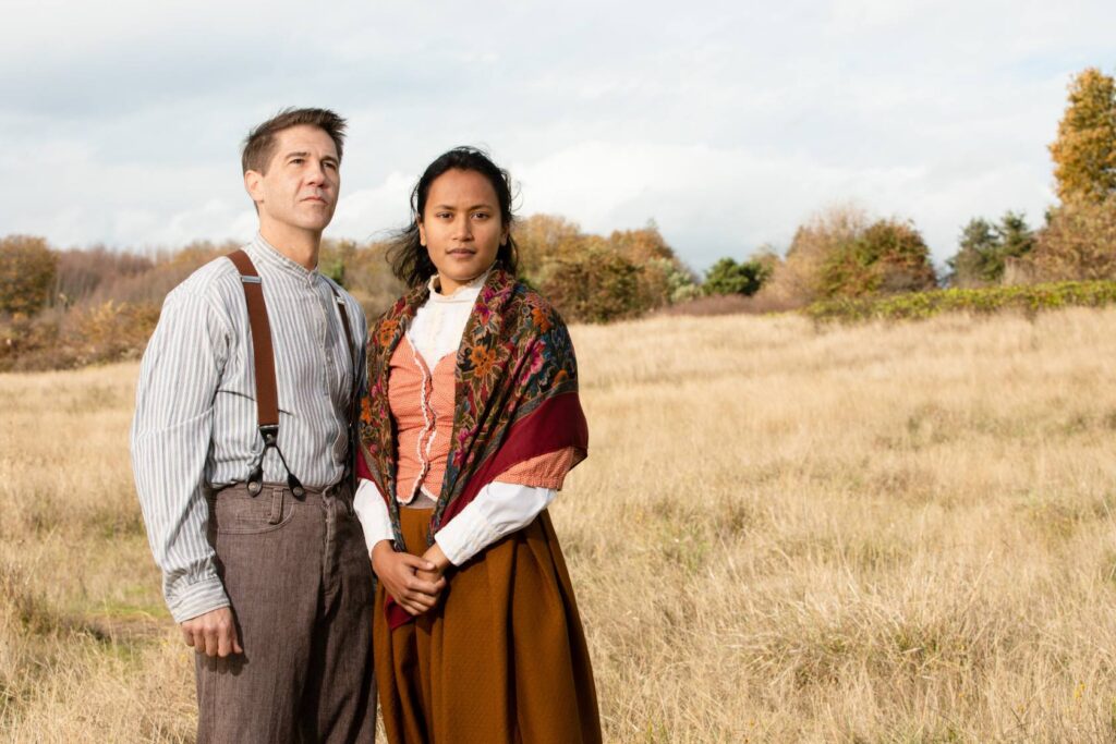 Two actors standing in an open field on a sunny day.