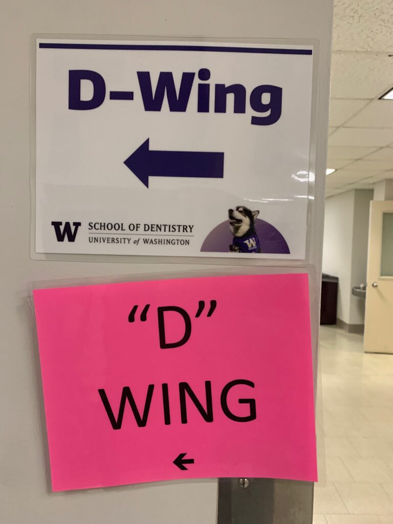 Two signs in a hallway pointing to the D-Wing on UW campus.